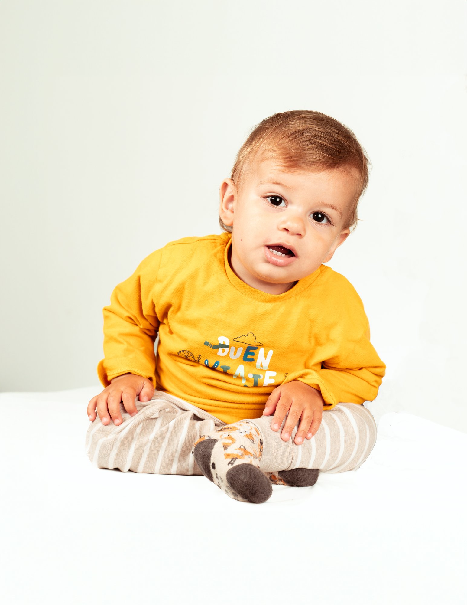 Colour portrait of a baby in a yellow jumper sitting on a studio backdrop